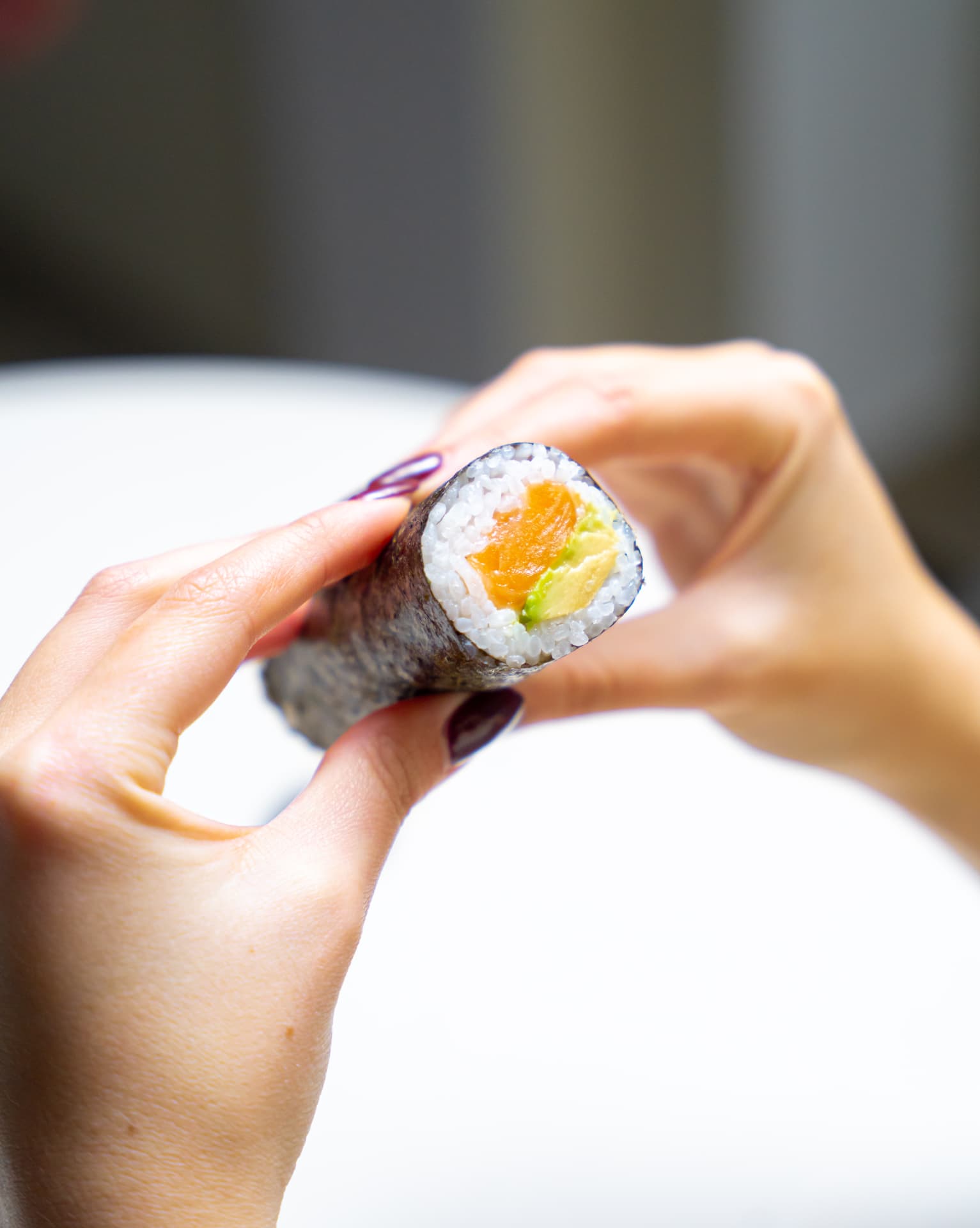 Hand holding a salmon avocado MAKU roll